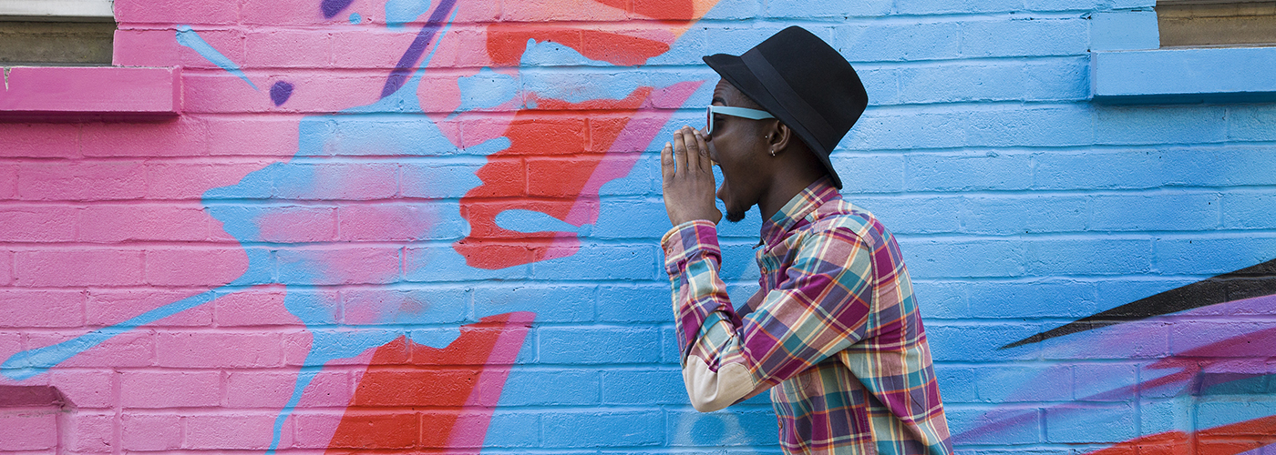 Homme de profil criant devant un graffiti coloré. 